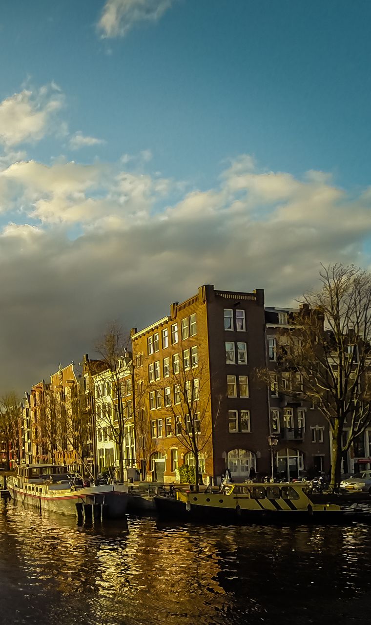 Grachtenpanden in Amsterdam in goudkleurig avondlicht, met woonboten aan de kade